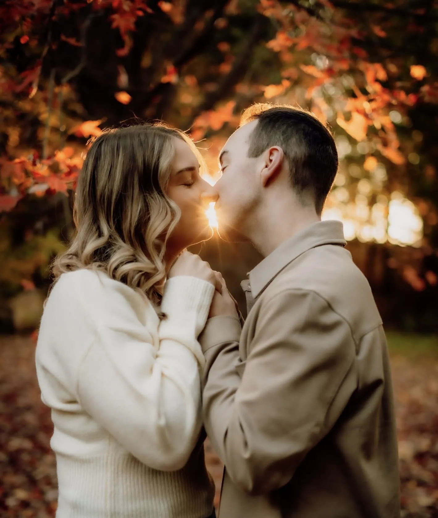 Couple kissing at golden hour beneath autumn maple leaves
